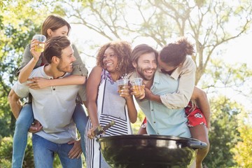 Men giving piggyback to women while preparing barbecue in park