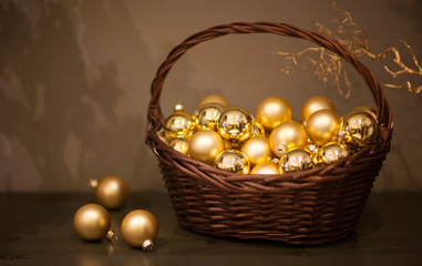 shiny and matt Christmas tree toys golden color in a wicker basket with a branch of the tree
