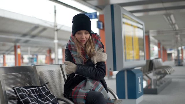 Girl looks ver vold and warming her hands while sitting on a platform
