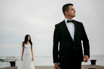 Thoughtful bride stands behind groom on the harbor