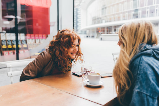 Two Young Beautiful Caucasian Blonde And Redhead Women Friends Having Breakfast Outdoor In A Bar - Friendship, Communication Concept