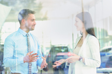 Obraz premium Two cheerful smiling young businesspeople talking at the office. View through window