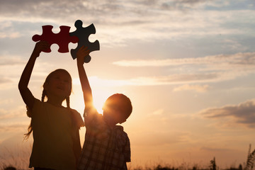 Silhouette of two happy children which playing on the field at t