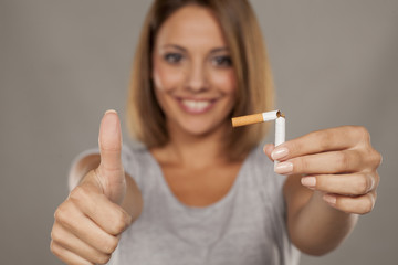 Obraz premium young happy woman holding a broken cigarette and showing thumbs up