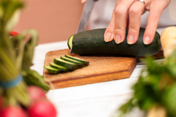 Housewife cutting cucumber with a knife in the kitchen