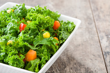Kale salad in bowl with carrot, pepper and sweet corn on wooden background
