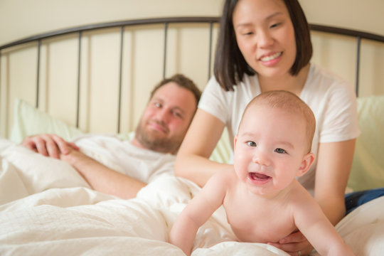 Young Mixed Race Chinese and Caucasian Baby Boy Laying In Bed with His Father and Mother.