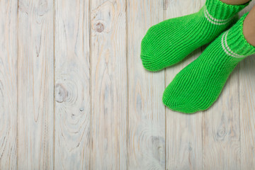 Female feet in knitted green socks on white wooden background.