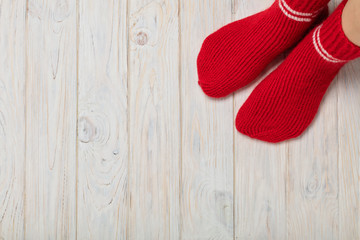 Female feet in knitted red socks on white wooden background.