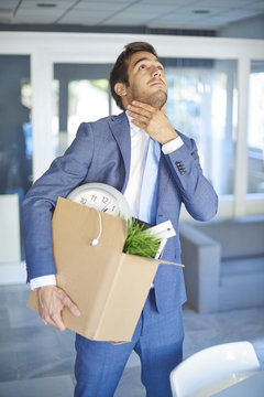 Shot of a young depressed businessman carrying cardboard box while leaving his workplace.
