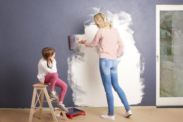 Shot of a woman and and her cute daughter painting the wall at home while renovation their home. 