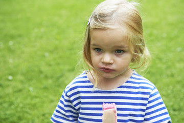 Beautiful little girl eats ice-cream in the summer with green grass background.

