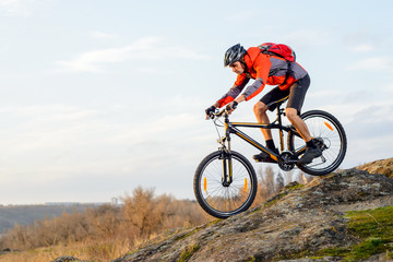 Fototapeta na wymiar Cyclist in Red Jacket Riding the Bike Down Rocky Hill. Extreme Sport.