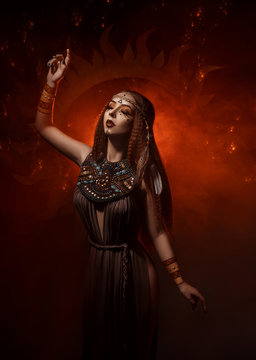 Beautiful, red-haired girl - a priestess of the sun. Dress and jewelry in ethnic style. Unusual make-up in orange and gold tones. Girl praying in silence.  Fantastic photography