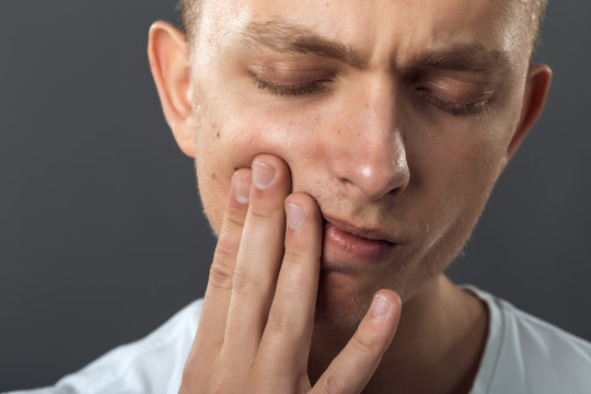 Close up portrait of a handsome man having toothache  standing on gray background