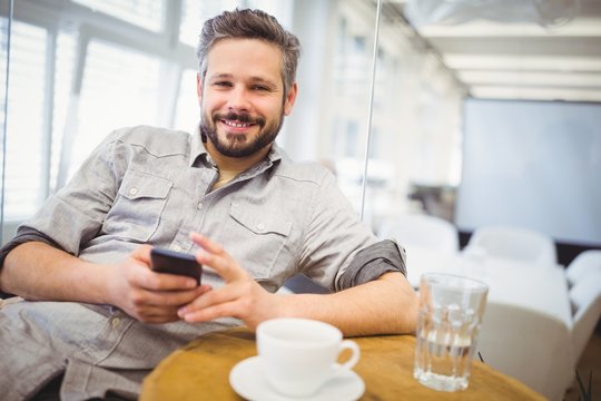 Smiling businessman using mobile phone in creative office