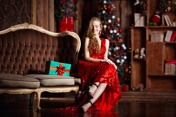 Holidays, celebration and people concept - young smiling woman in elegant red dress over christmas...