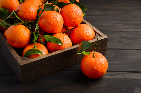 Fresh tangerine clementine with leaves on dark wooden background, selective focus, horizontal with copy space.