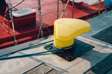 Mooring bollard on a wooden pier with docked red boat on the background