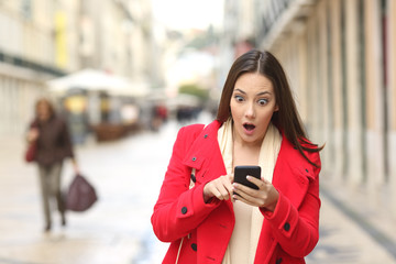 Amazed woman checking smart phone in the street