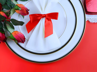 Simple place setting for Valentine's Day with black and white china, silk red roses, a bow on a red...
