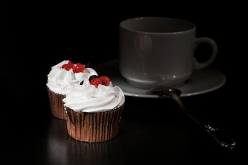 Two white cakes from cream with red berry on top on dark background with white cup and spoon/different cake position