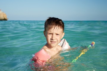 Boy with floater  sleeves swimming in a sea and having fun with water pistol