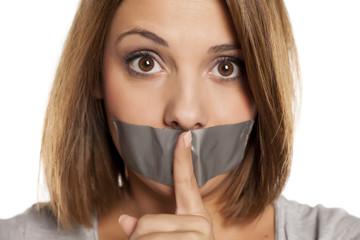 angry young woman with adhesive tape over her mouth, and finger in front of the tape
