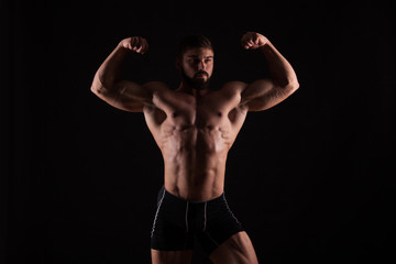 Fototapeta na wymiar Rear view of healthy muscular young man with his arms stretched out isolated on black background