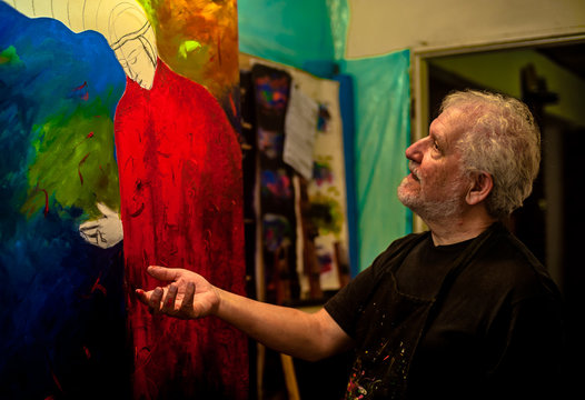 Homem idoso, de cabelos e barba brancos,  artista, pintor, trabalhando em seu atelier