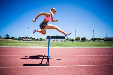Female athlete jumping above the hurdle - Powered by Adobe