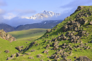 Green hill with rocks and Balyk Subashi peak (3932 m) in the Caucasus