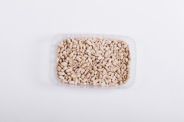 Plastic container with roasted peanuts on a white background