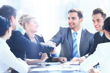 Business colleagues sitting at a table during a meeting with two male executives shaking hands
