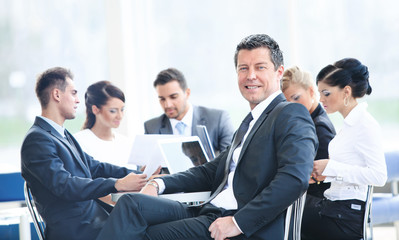 Portrait of young handsome businessman in office with colleagues in the background