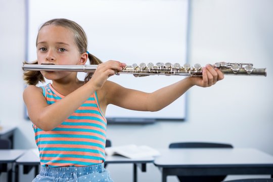 Portrait of elementary girl playing flute in classroom