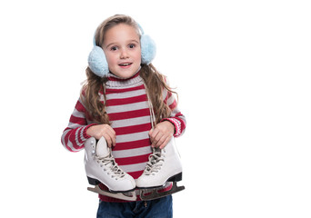 Lovely smiling little girl wearing colorful striped sweater and headdress, holding skates isolated on white background. Winter clothes.