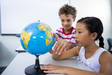 Elementary boy and girl looking at glob in classroom