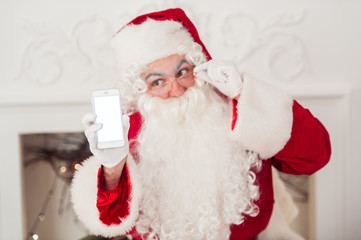 Obraz na płótnie Canvas Santa Claus shows a smartphone with fireplace at background