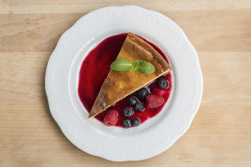 Piece of cheesecake with raspberry puree on white plate