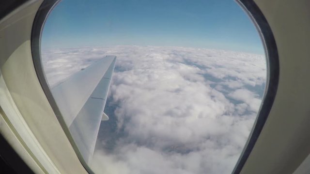 View Out of Commercial Jet Airliner Window while Flying Over White Clouds in a Blue Sky on a Sunny Day