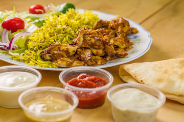 Close-up photo of chicken shawarma plate, juicy and fresh middle-eastern food. Pita bread and rice along with yogurt, ketchup, and hummus. 