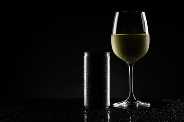A chilled glass of white wine and a can, sparkling wine on a reflective and dark background