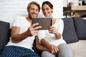 Fototapeta premium Beautiful couple looking at tablet smiling sitting on sofa home.
