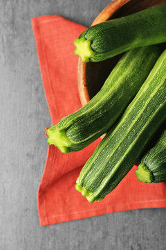 Composition with fresh zucchini in wooden bowl and napkin on gray background