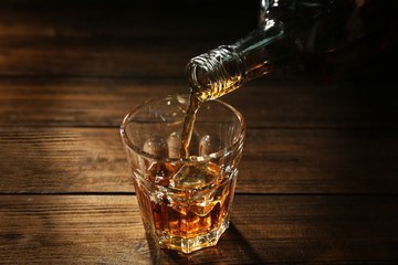 Pouring whisky into glass on wooden table closeup