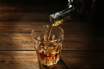 Foto op Canvas Pouring whisky into glass on wooden table closeup © Africa Studio