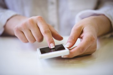 Close-up of businesswoman touching cellphone on desk at office