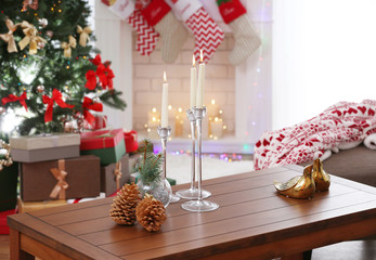 Cones, candles and Christmas decor on wooden table against fireplace