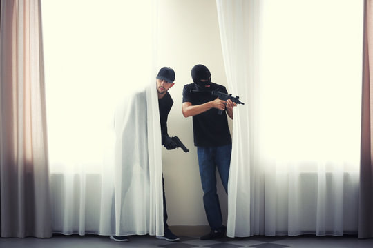 Male thieves with gun behind curtains